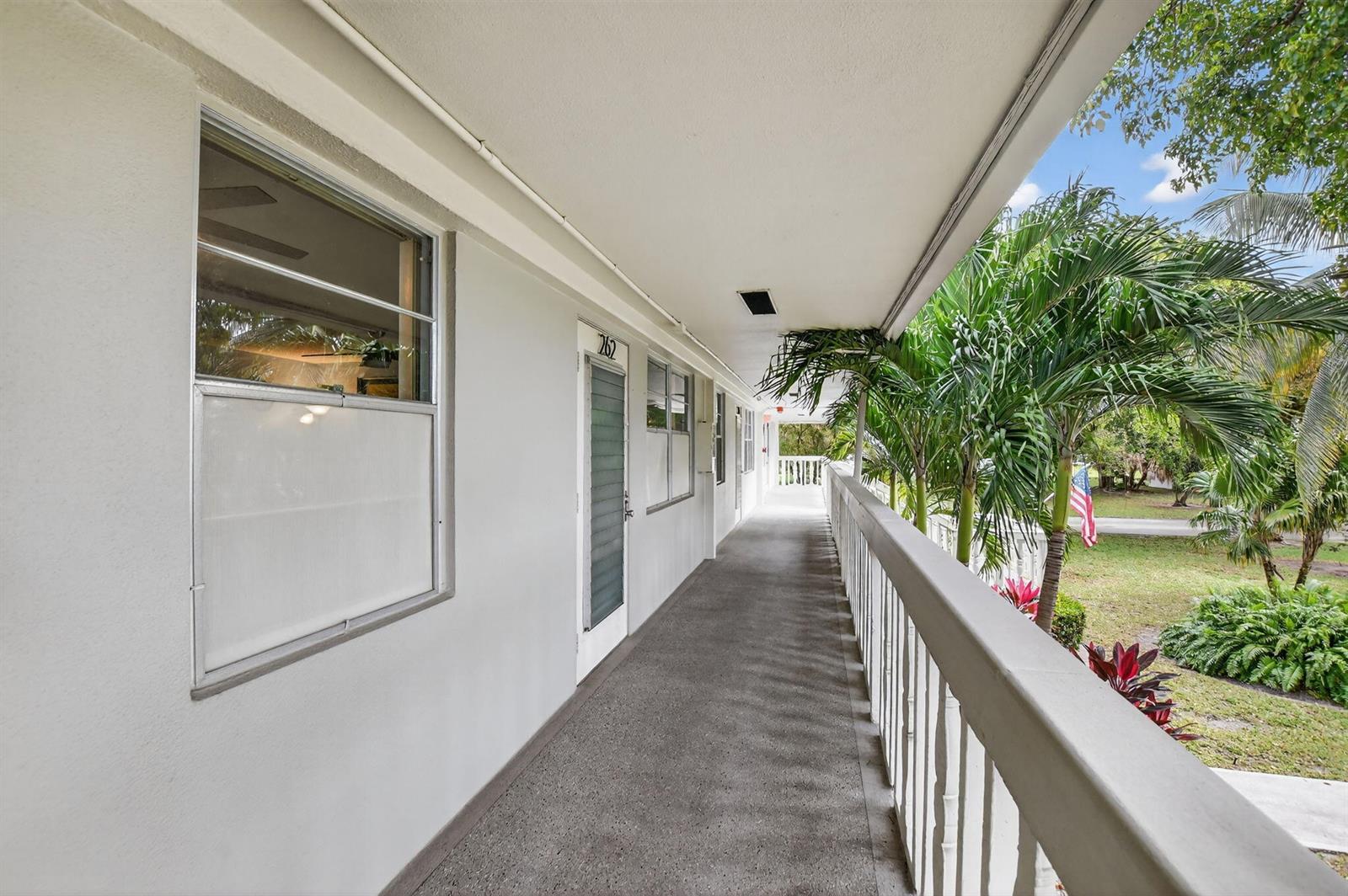 An outdoor walkway with a concrete floor and white railing overlooks a grassy yard — 262 Ventnor R, Deerfield Beach FL 33442, DEERFIELD BEACH, FL
