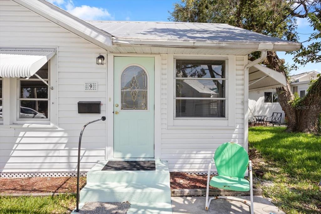 A white house exterior features a light green front door, a metal roof, and a chair — 9 SEMINOLE DRIVE, BRADENTON, FL