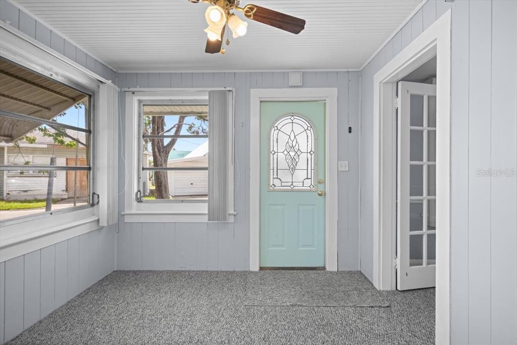 A sunroom features light blue paneled walls, gray carpeting, a ceiling fan, and a glass-paneled door — 9 SEMINOLE DRIVE, BRADENTON, FL