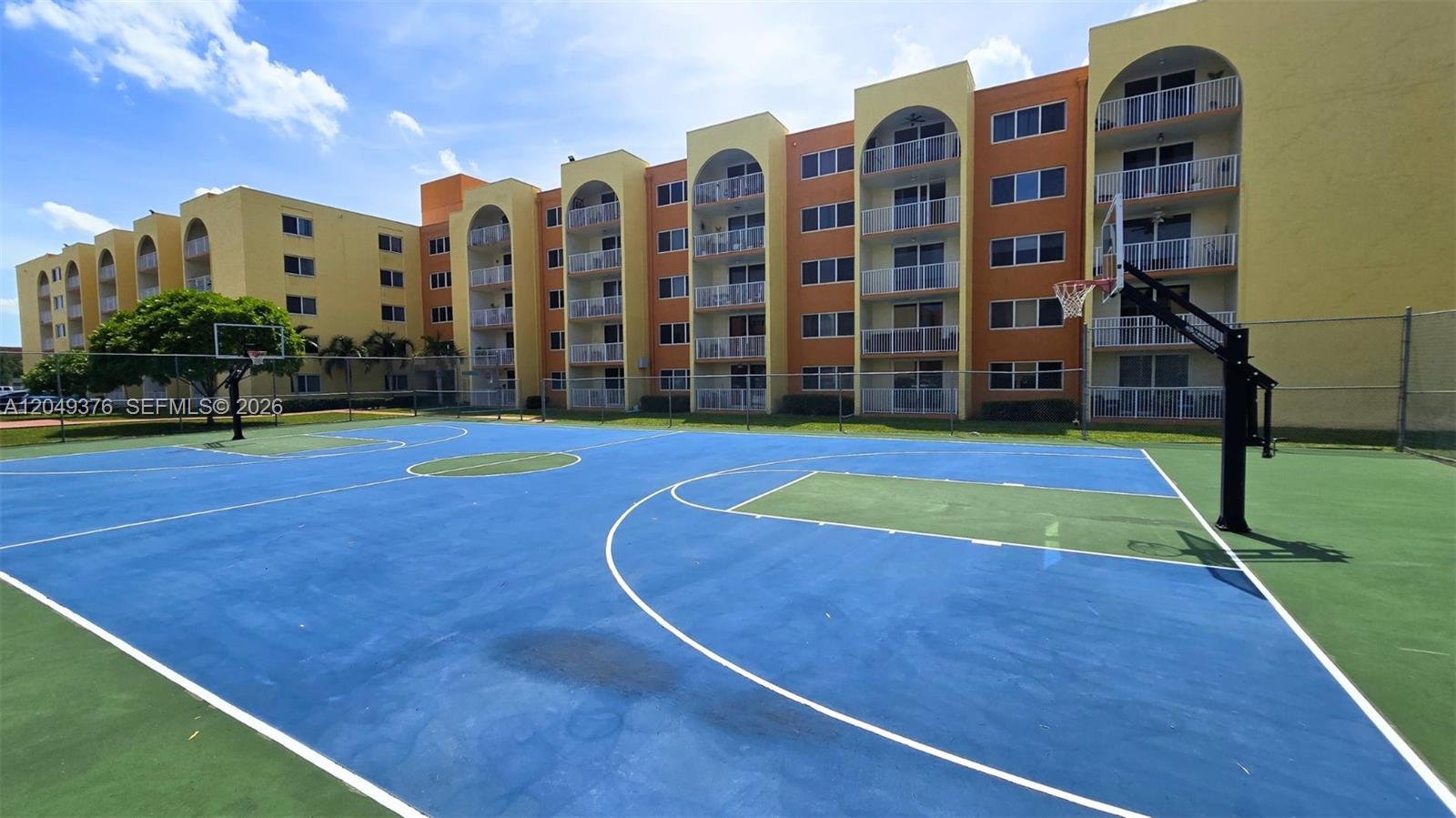 An outdoor basketball court sits in front of a multi-story yellow and orange apartment building — HIALEAH, FL