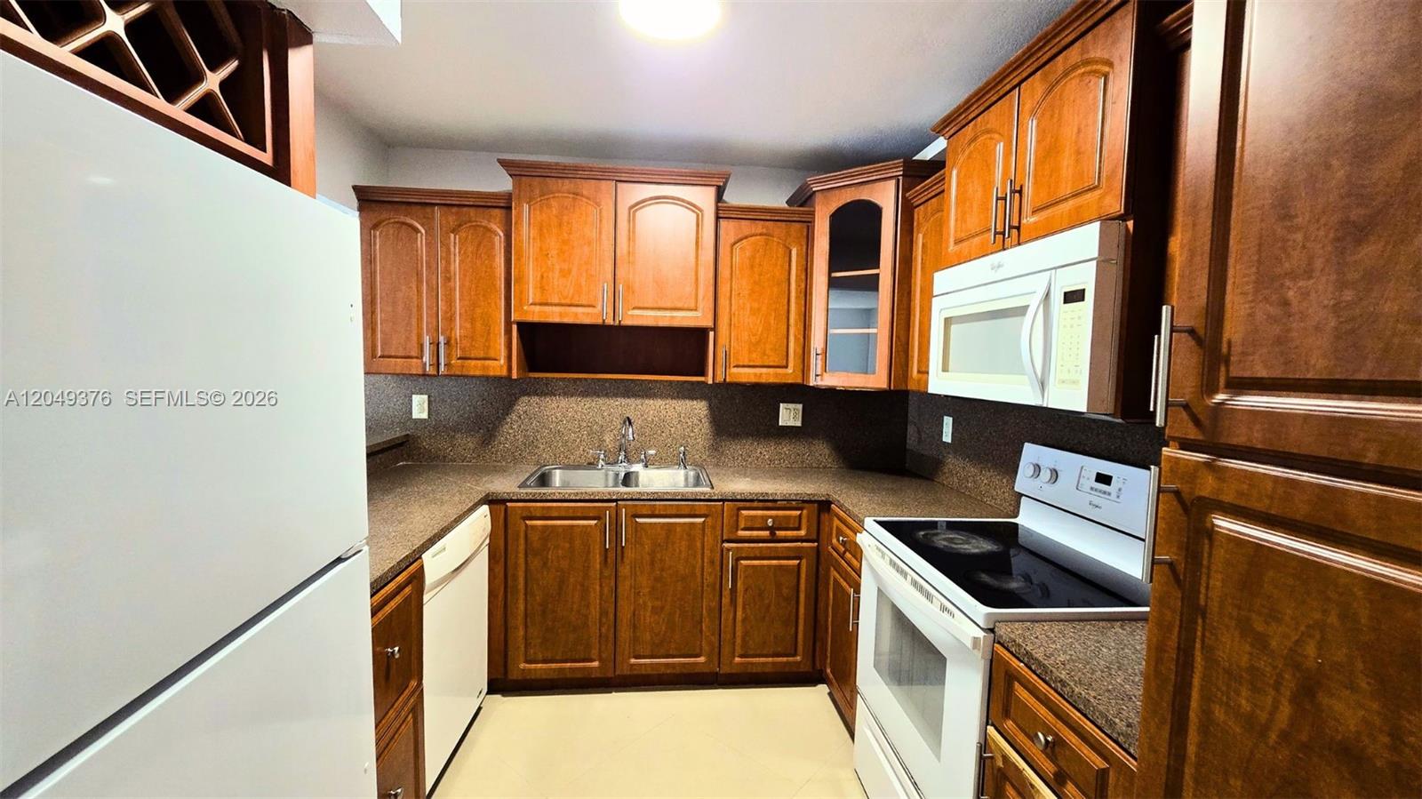 A kitchen features wood cabinets, granite countertops, and white appliances — HIALEAH, FL