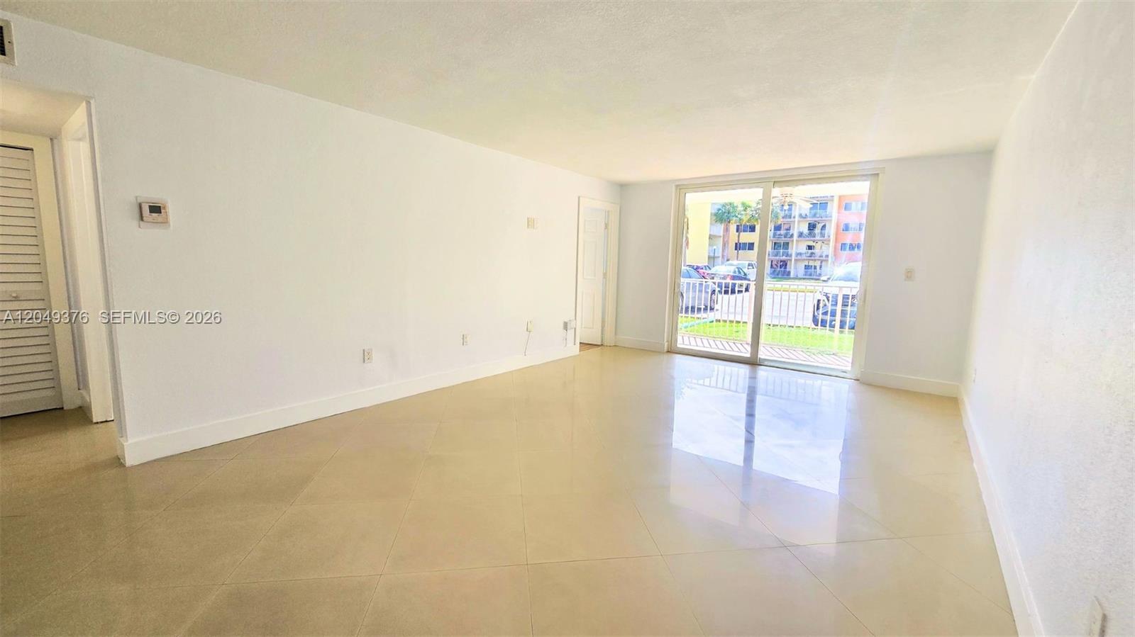 An empty living room features light-colored tile flooring, white walls, and a sliding glass door — HIALEAH, FL