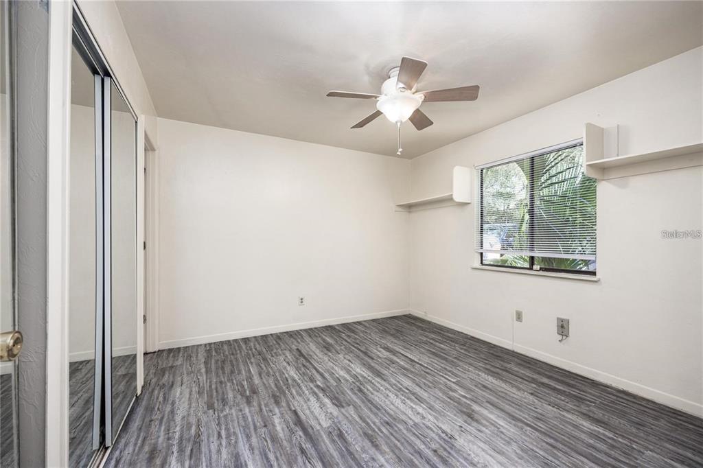An empty bedroom features gray wood-look flooring, a ceiling fan, and white wall-mounted shelves — 127 SE 16TH AVENUE UNIT S-105, GAINESVILLE, FL