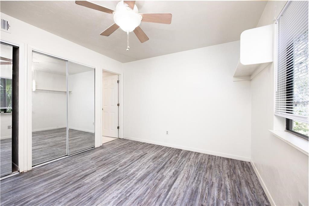 An empty bedroom features wood-look flooring, a ceiling fan, mirrored closet doors, and white walls — 127 SE 16TH AVENUE UNIT S-105, GAINESVILLE, FL