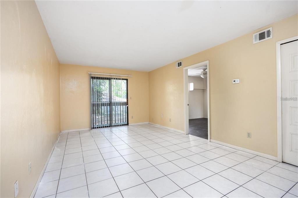 An empty room with white tile flooring, beige walls, and a sliding glass door — 127 SE 16TH AVENUE UNIT S-105, GAINESVILLE, FL