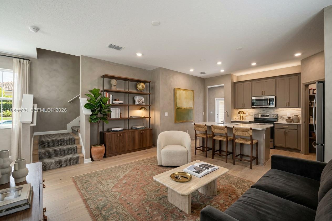 A modern open-concept living room and kitchen featuring wood flooring, a bookshelf, and island seating — 6349 Blissful Street, Clermont FL 34714, CLERMONT, FL