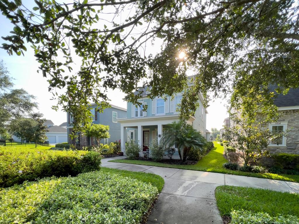 A two-story light blue house with a front porch sits along a concrete sidewalk — 5912 VILLAGE CENTER DRIVE, LITHIA, FL