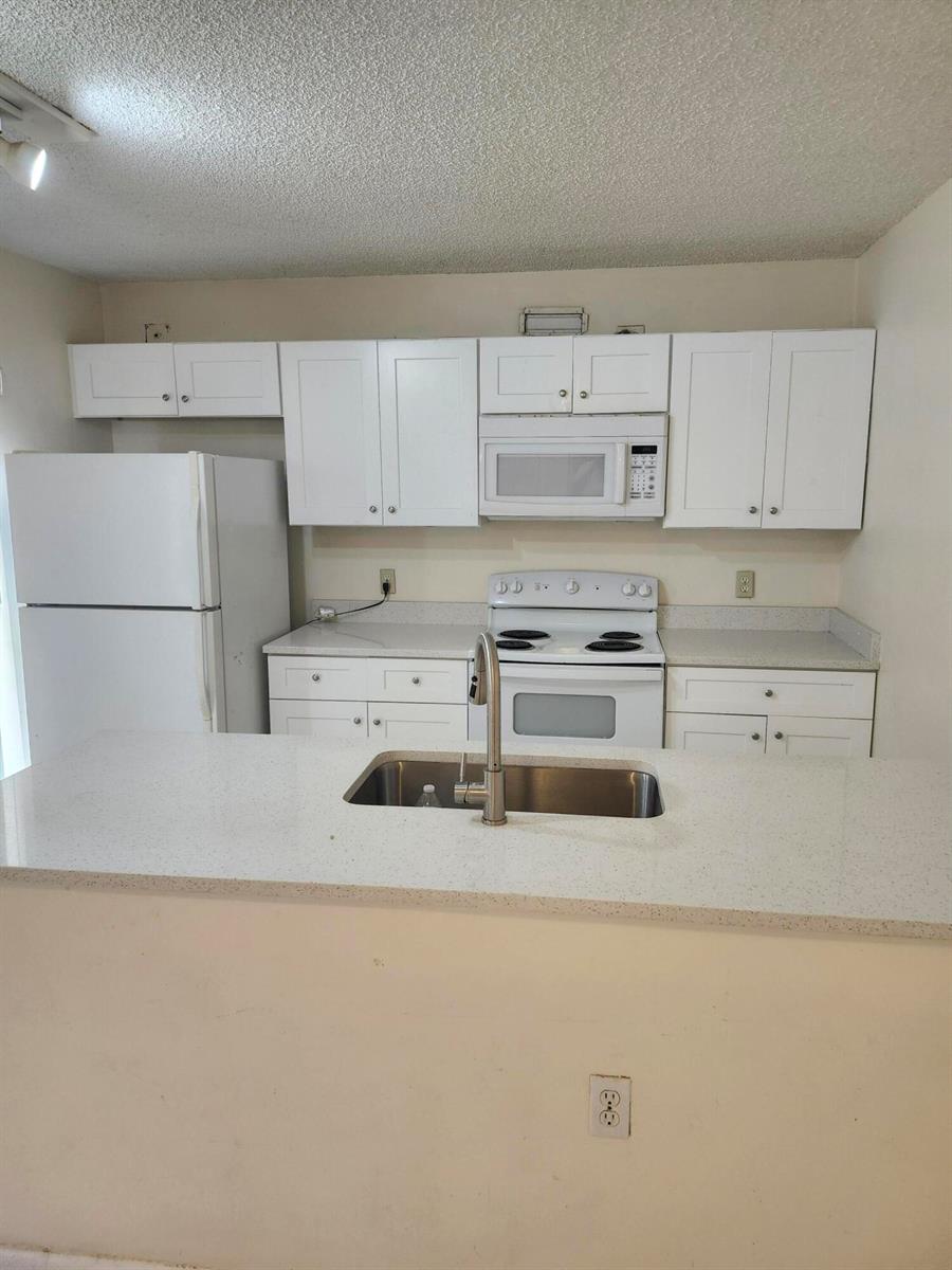 A kitchen features white cabinets, white appliances, and a peninsula with a stainless steel sink — 1612 16th Way # 1612, West Palm Beach FL 33407, WEST PALM BEACH, FL