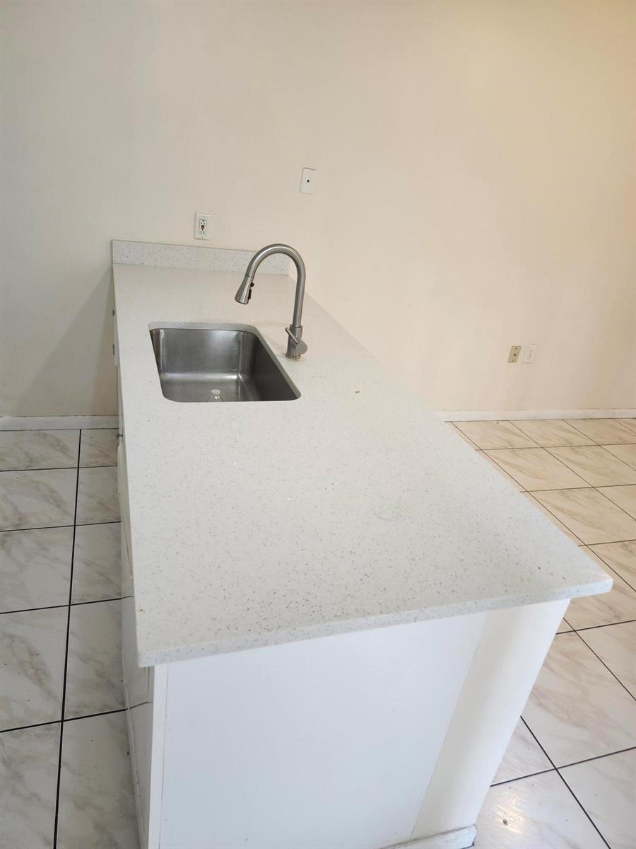 A kitchen island features a white speckled countertop, a stainless steel sink, and a faucet — 1612 16th Way # 1612, West Palm Beach FL 33407, WEST PALM BEACH, FL