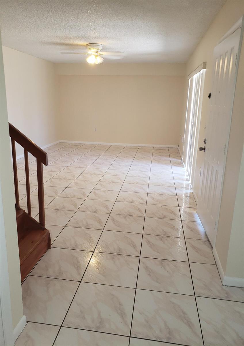 An empty room with light-colored tile flooring, a wooden staircase, and a ceiling fan — 1612 16th Way # 1612, West Palm Beach FL 33407, WEST PALM BEACH, FL