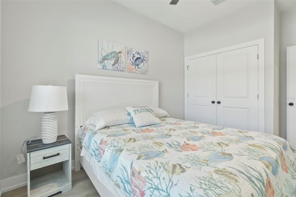 A bedroom features a white bed with patterned bedding, a nightstand, and a closet — 9155 AGATE STREET UNIT 9155, PORT CHARLOTTE, FL