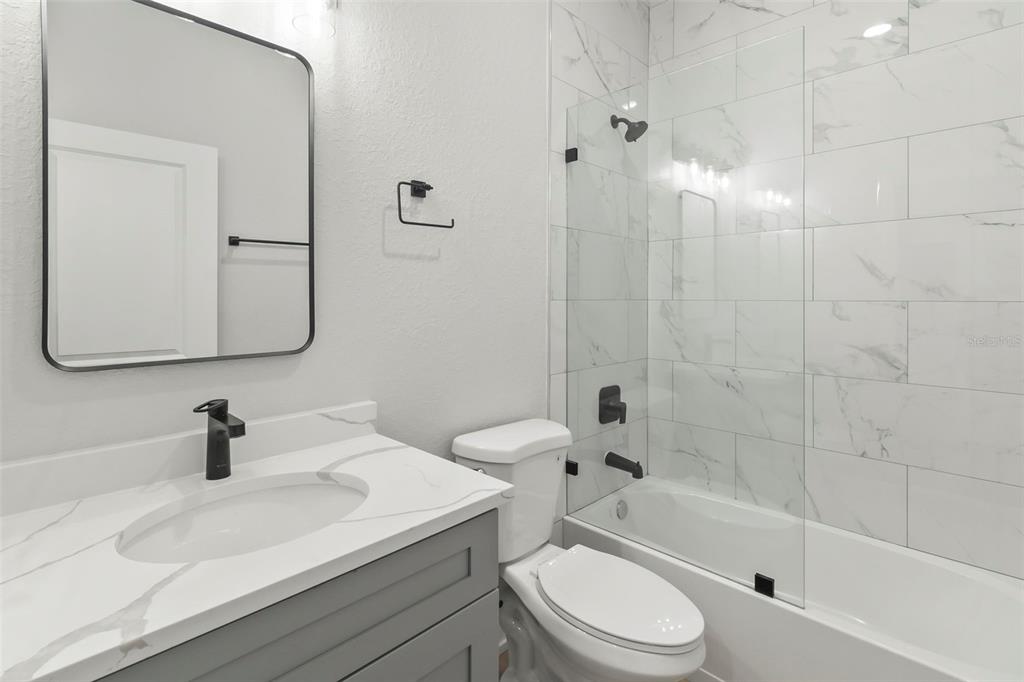 A modern bathroom features a gray vanity, marble-look countertop, and a glass-enclosed shower-tub combination — 9155 AGATE STREET UNIT 9155, PORT CHARLOTTE, FL