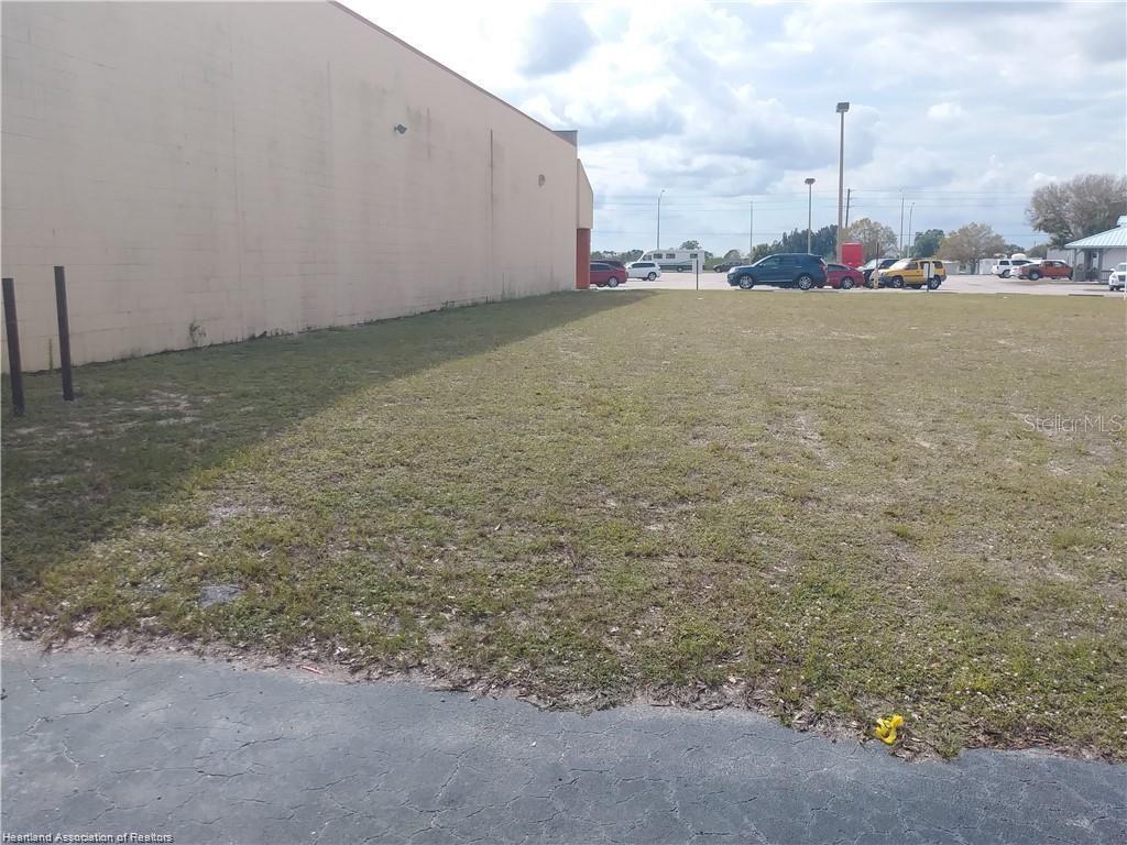 A large, empty grassy lot sits adjacent to the side of a beige commercial building — 115 COUNTY ROAD 29, LAKE PLACID, FL