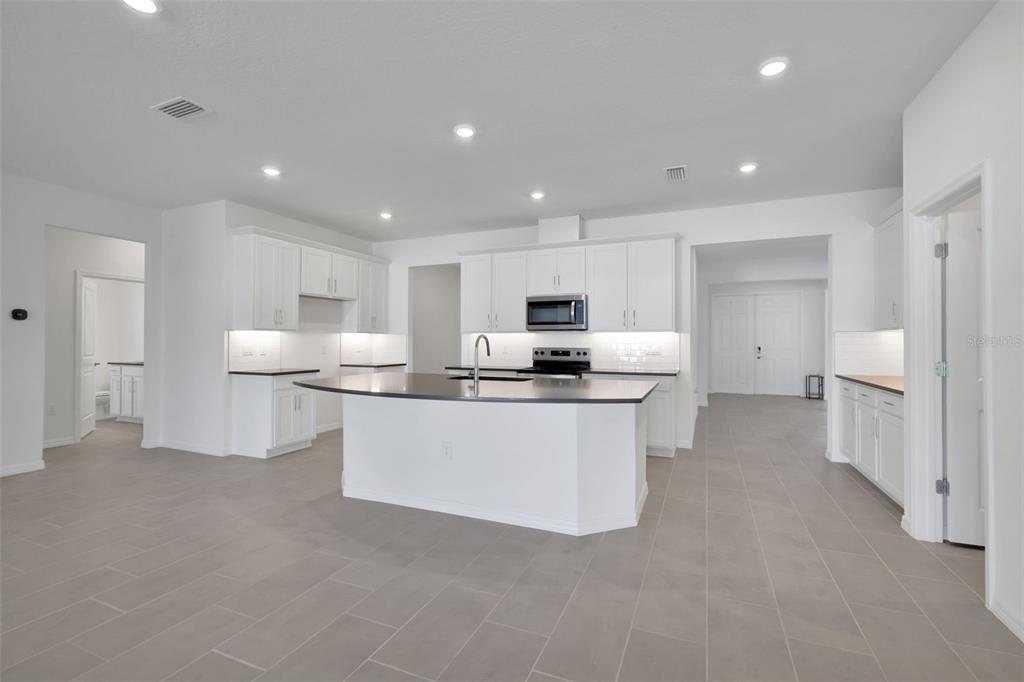 A modern kitchen features white cabinetry, a large central island, and gray tile flooring — 17534 VALLEYWOOD PARKWAY, LAND O LAKES, FL