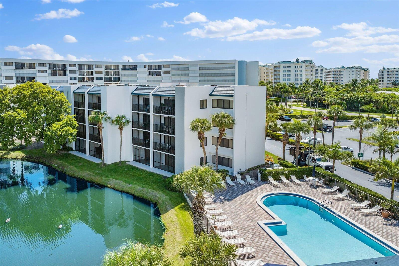 An aerial view shows a multi-story apartment building next to a swimming pool and pond — 1605 S Us Hwy 1 # E104, Jupiter FL 33477, JUPITER, FL