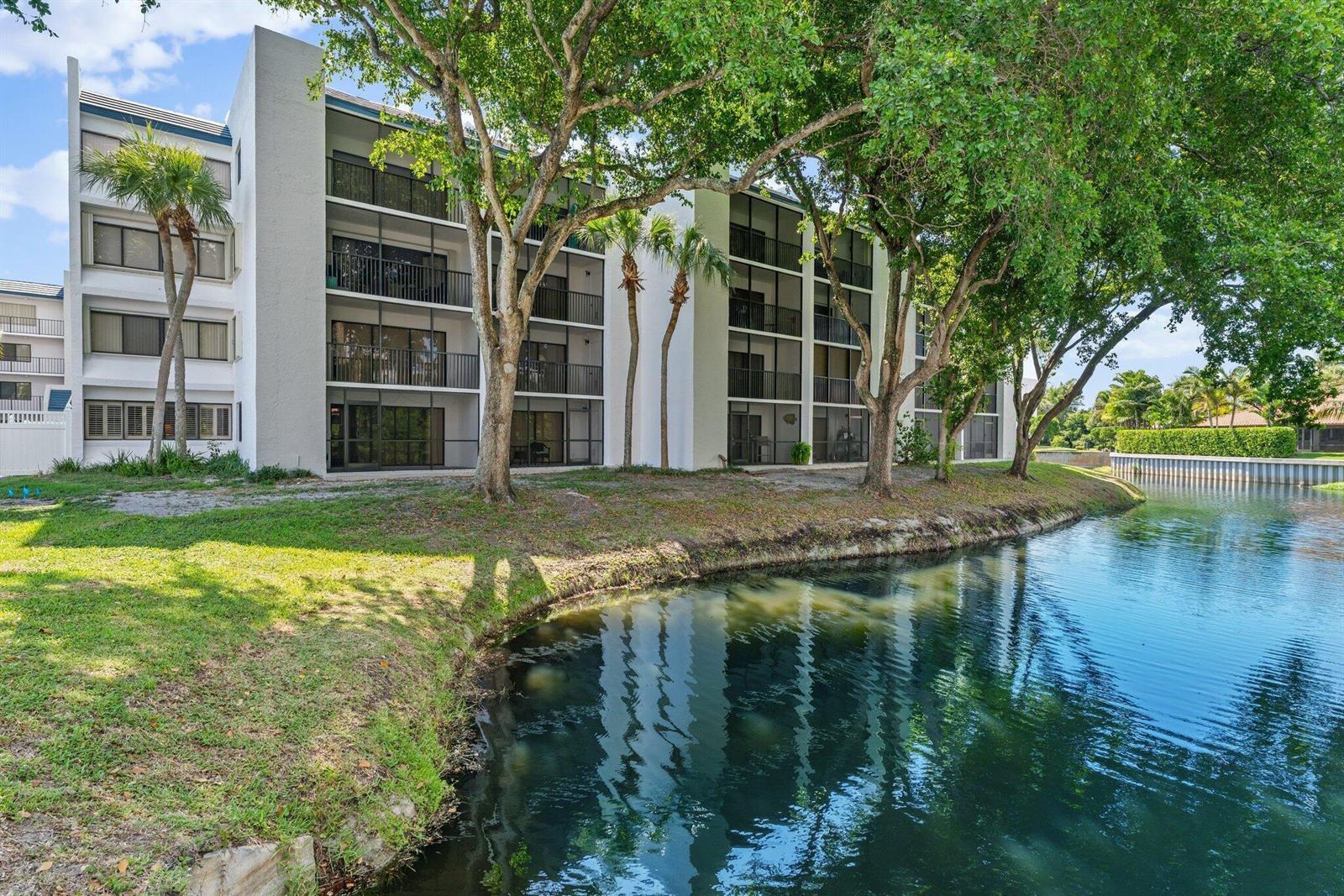 A multi-story apartment building sits beside a canal surrounded by trees and grass — 1605 S Us Hwy 1 # E104, Jupiter FL 33477, JUPITER, FL