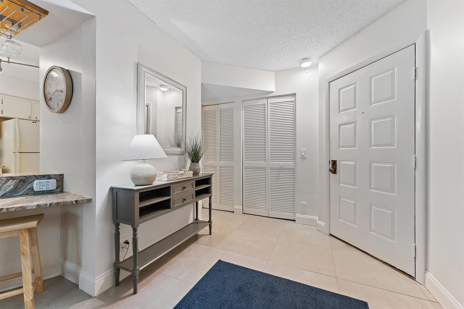 An entryway features a gray console table, a mirror, louvered closet doors, and tile flooring — 1605 S Us Hwy 1 # E104, Jupiter FL 33477, JUPITER, FL