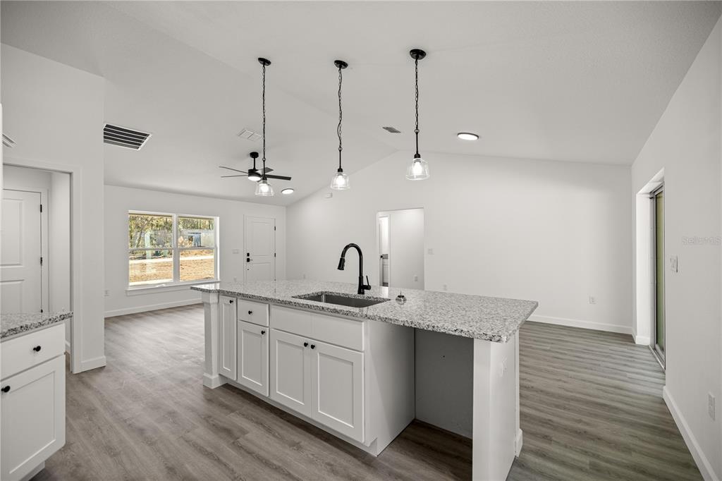 An open-concept living area features light wood-look flooring, a kitchen island, and sliding glass doors — 24125 NW FOXGLOVE LANE, DUNNELLON, FL