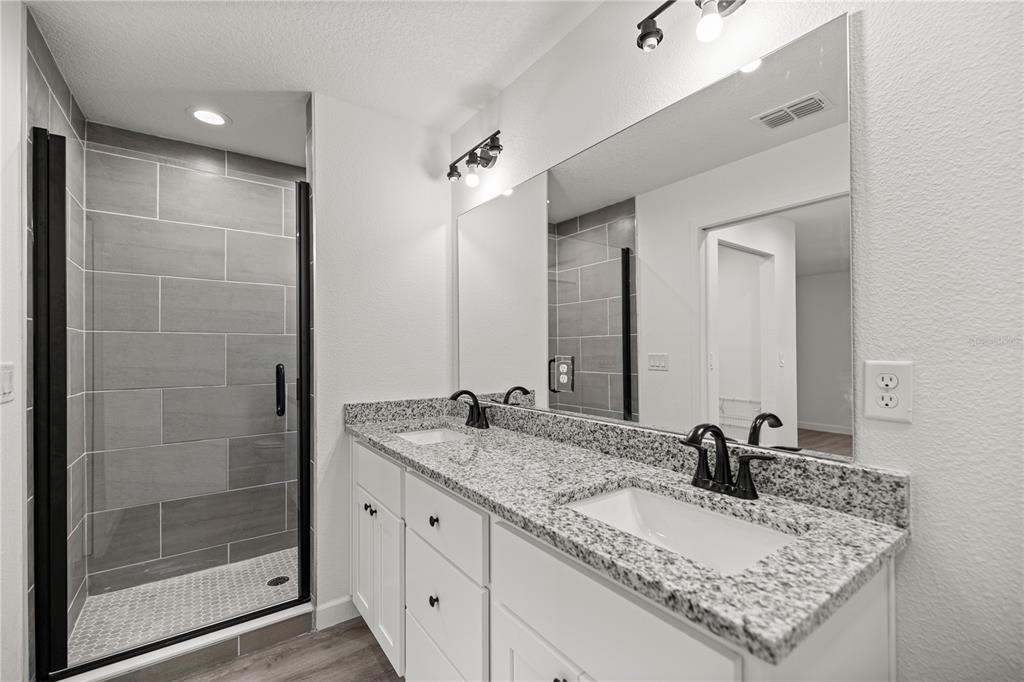 A bathroom features a double vanity with granite countertops, white cabinets, and a tiled shower — 24125 NW FOXGLOVE LANE, DUNNELLON, FL
