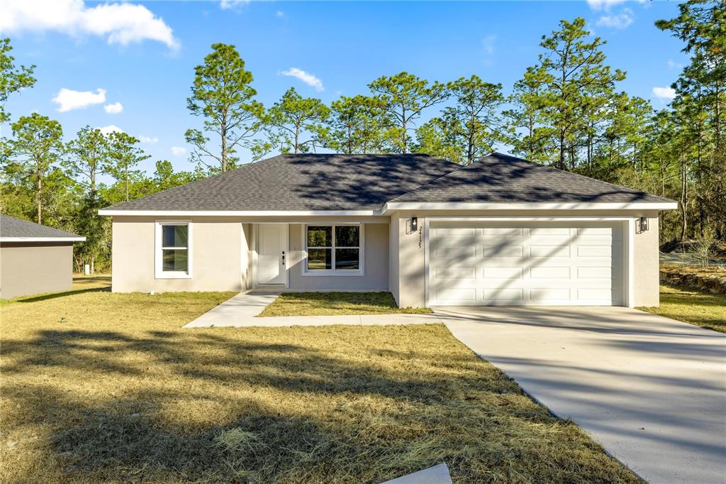 A single-story house with a beige stucco exterior, a dark shingled roof, and a garage — 24125 NW FOXGLOVE LANE, DUNNELLON, FL