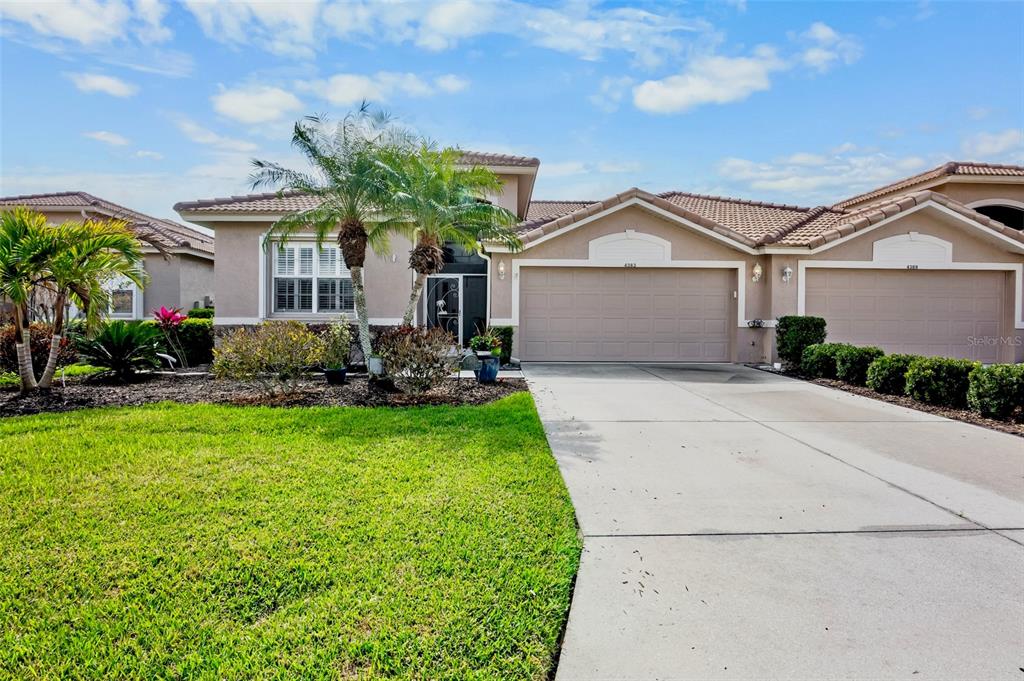 A single-story suburban house with a tan stucco exterior, two garage doors, and palm trees — 4383 SAMOSET DRIVE, SARASOTA, FL