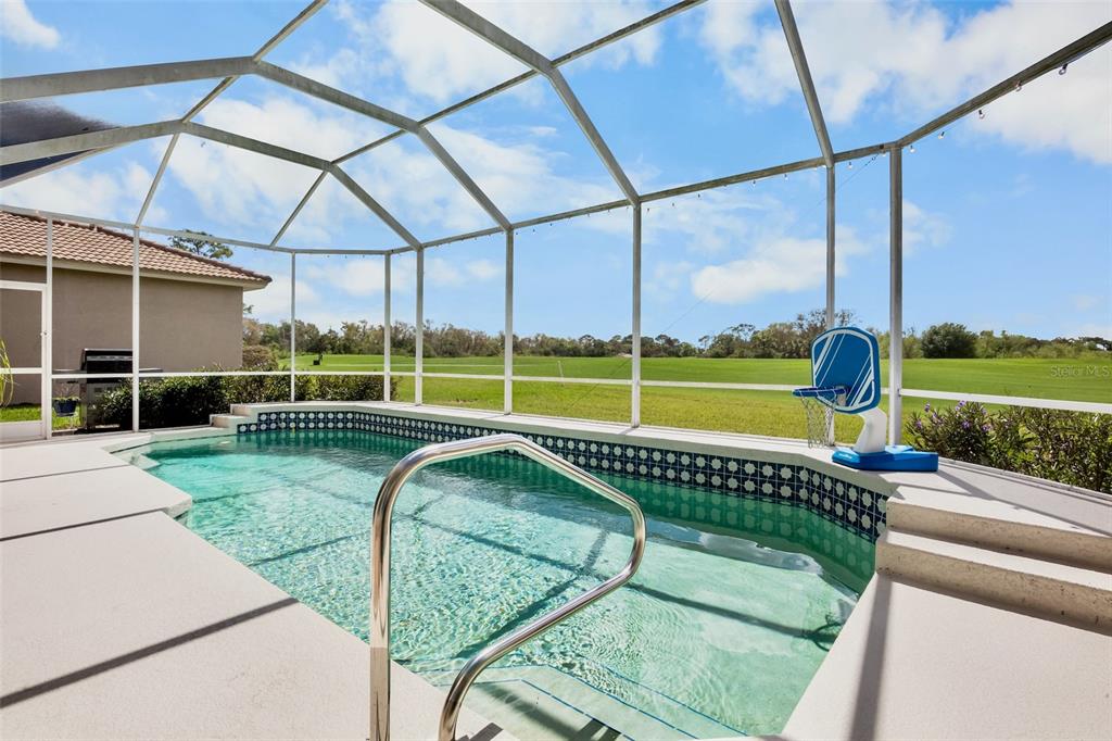 A screened-in swimming pool overlooks a grassy golf course under a blue sky — 4383 SAMOSET DRIVE, SARASOTA, FL