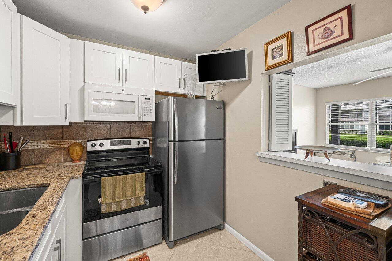 A kitchen features white cabinets, granite countertops, stainless steel appliances, and a pass-through window — 175 Suffolk E, Boca Raton FL 33434, BOCA RATON, FL