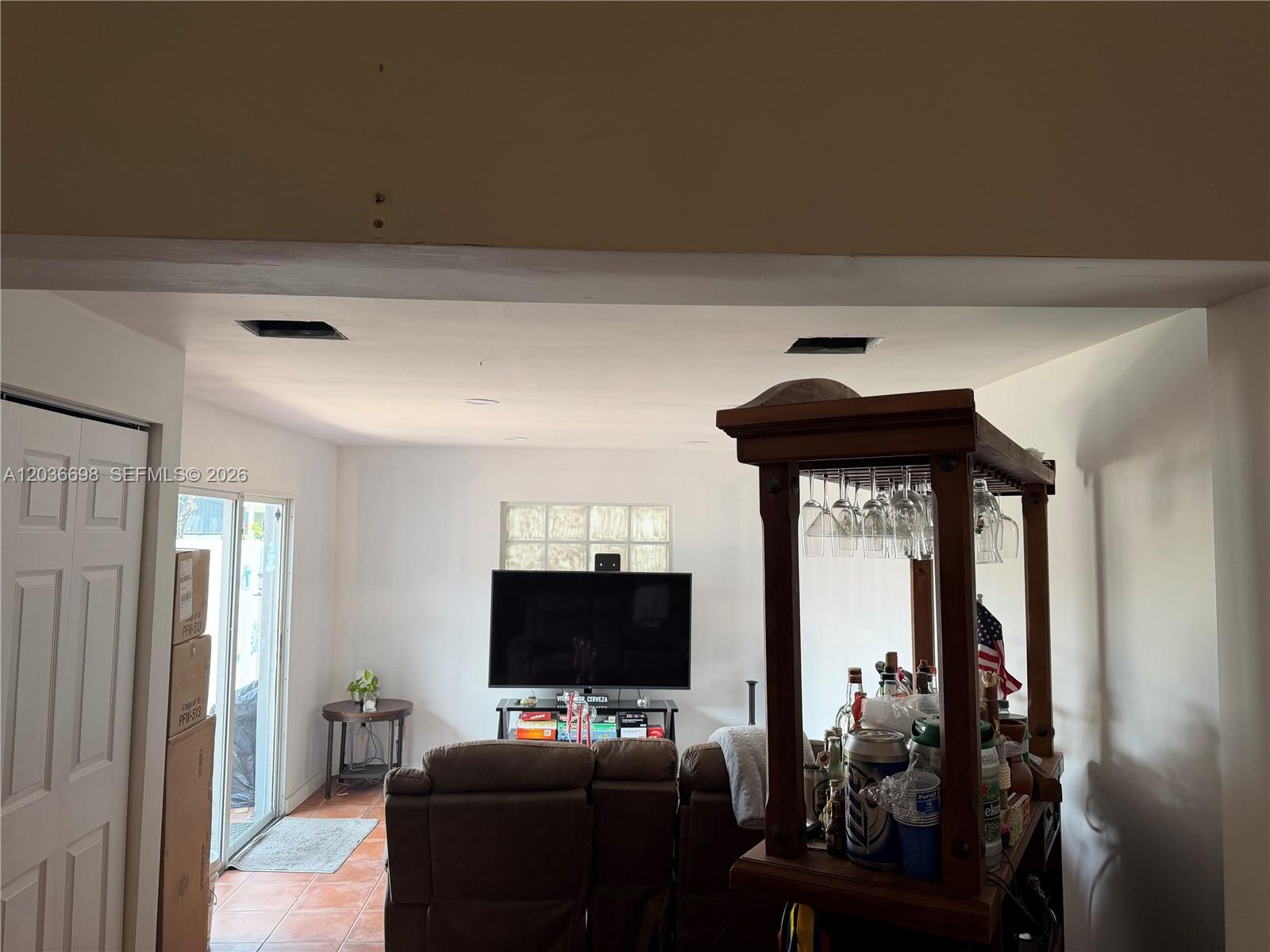 A living room features a television, a brown sofa, and a wooden bar unit — MIAMI, FL