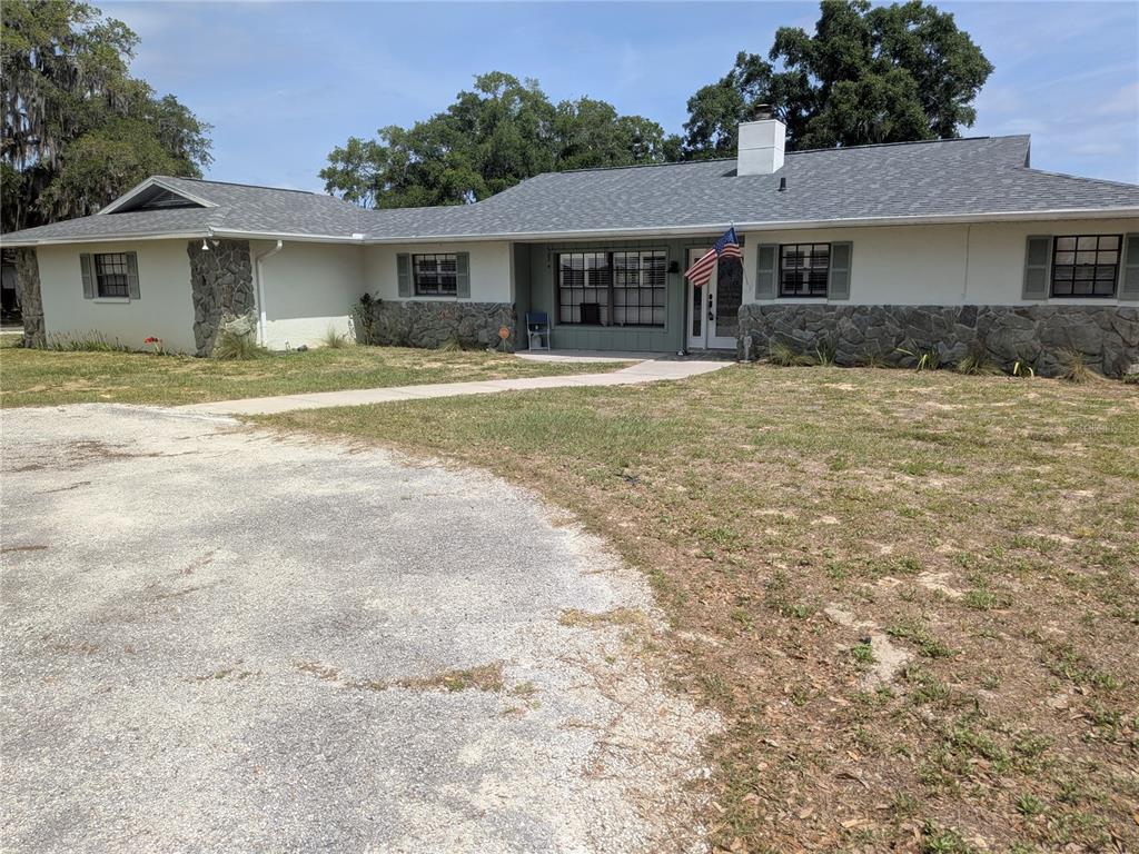 A single-story house with a stone facade, gray roof, and a gravel driveway — 8801 E CRESCO LANE, INVERNESS, FL