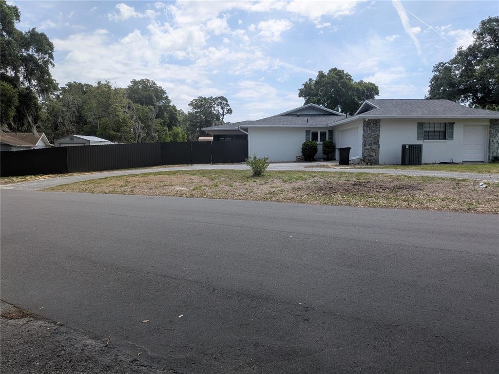 A single-story house with a white exterior and a dark privacy fence sits near a road — 8801 E CRESCO LANE, INVERNESS, FL