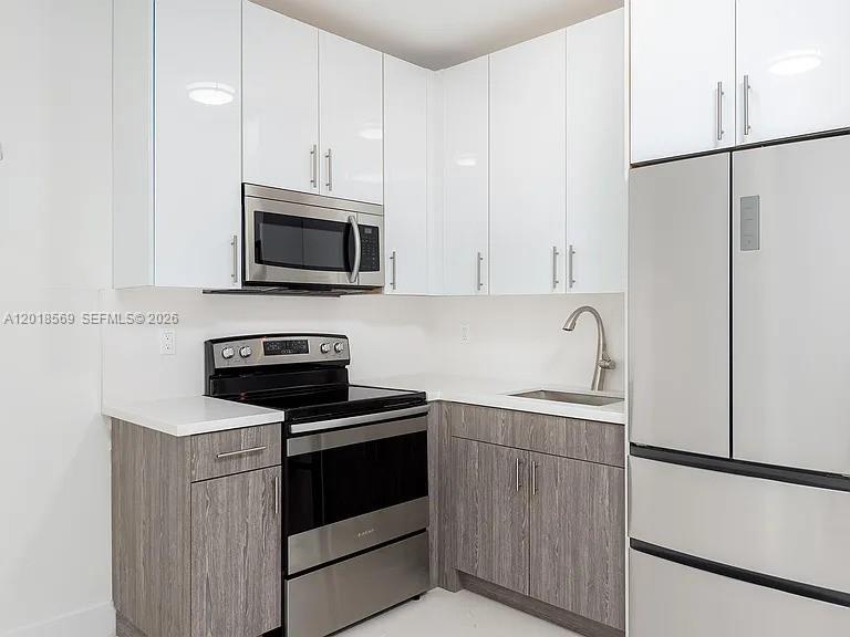 A modern kitchen features white upper cabinets, wood-grain lower cabinets, and stainless steel appliances — 676 NW 47th St # 5, Miami FL 33127, MIAMI, FL