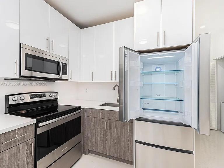A modern kitchen features white upper cabinets, wood-grain lower cabinets, and stainless steel appliances — 676 NW 47th St # 5, Miami FL 33127, MIAMI, FL