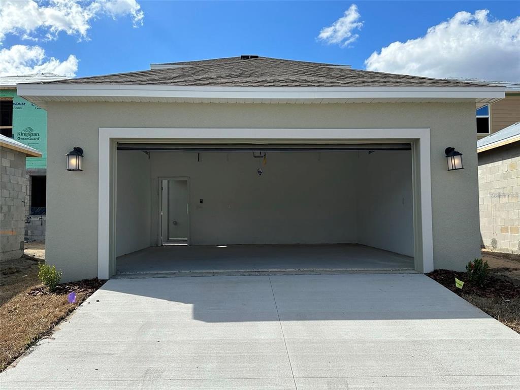 An exterior view of a two-car garage with a concrete driveway and two wall lamps — 6014 BLISSFUL STREET, CLERMONT, FL