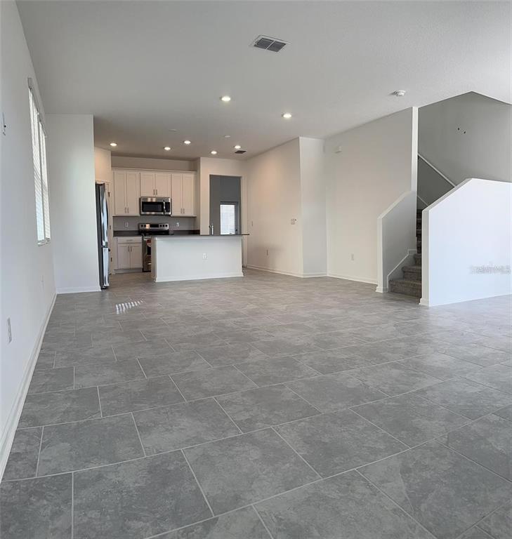 An open-concept kitchen and living area features gray tile flooring and a staircase — 6014 BLISSFUL STREET, CLERMONT, FL