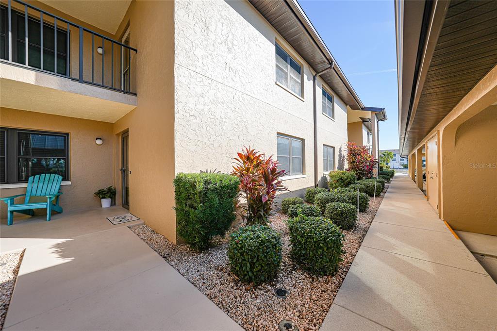 A tan apartment building exterior features a ground-level patio, a balcony, and landscaped bushes — 240 LEWIS CIRCLE UNIT 513, PUNTA GORDA, FL