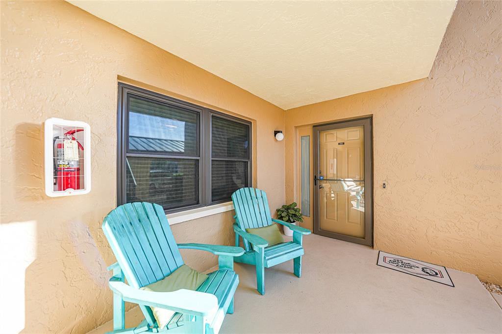 A covered patio features two light blue Adirondack chairs, a fire extinguisher, and a front door — 240 LEWIS CIRCLE UNIT 513, PUNTA GORDA, FL