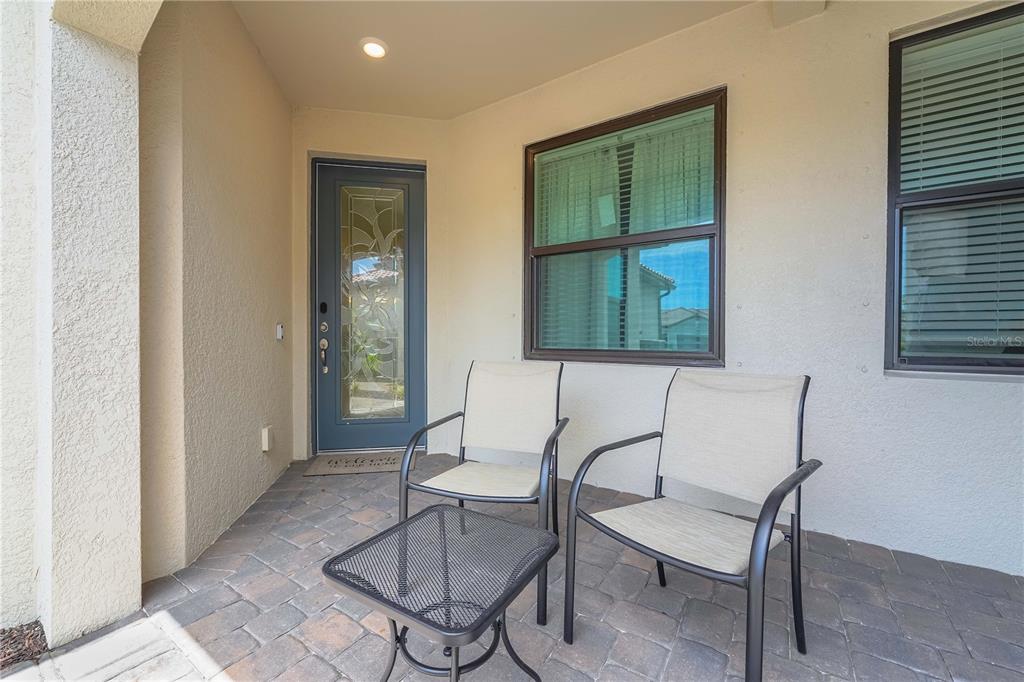 A covered entryway features a paved floor, two chairs, a small table, and a glass-paneled door — 14574 MOSSY PINE COURT, NOKOMIS, FL