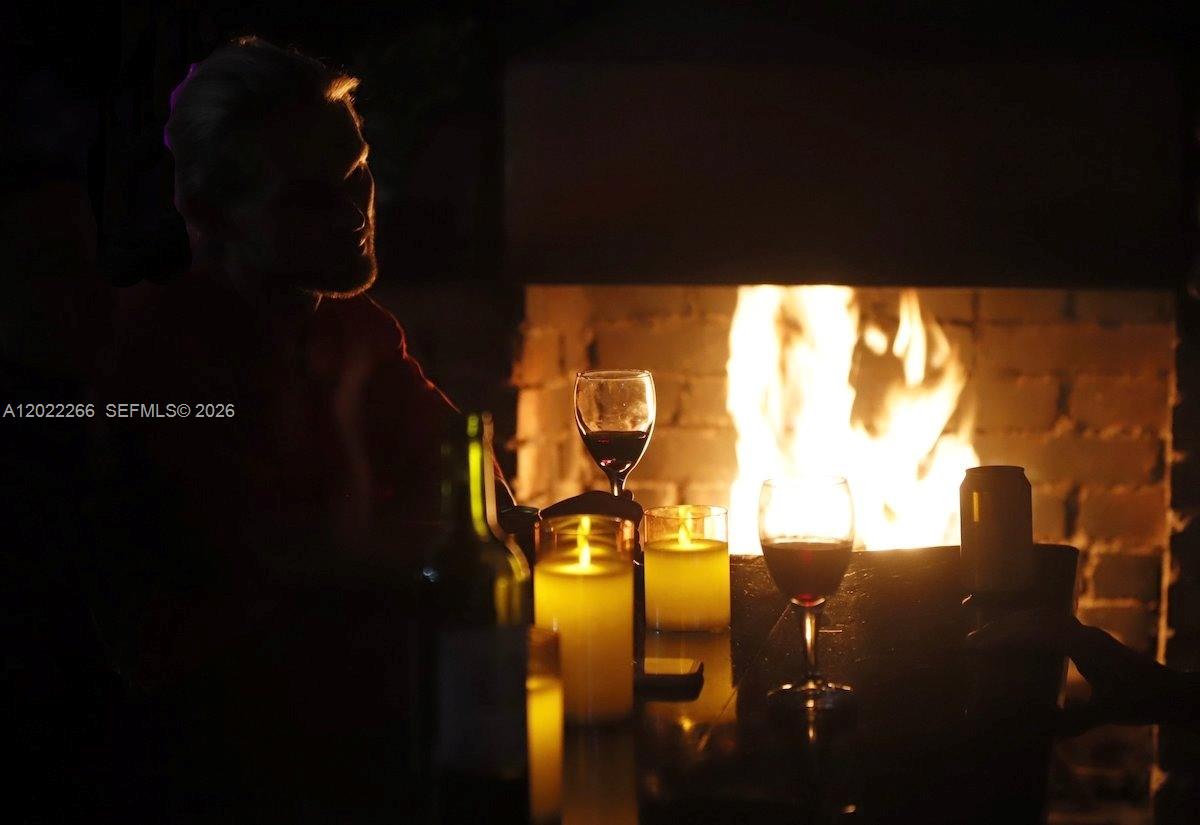 A person sits by a fireplace with wine glasses and candles on a table — X Carretera, 00000, FL