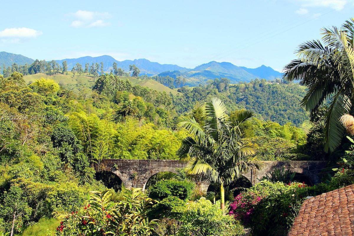 A stone arched bridge spans a lush, green valley beneath a backdrop of distant mountains — X Carretera, 00000, FL