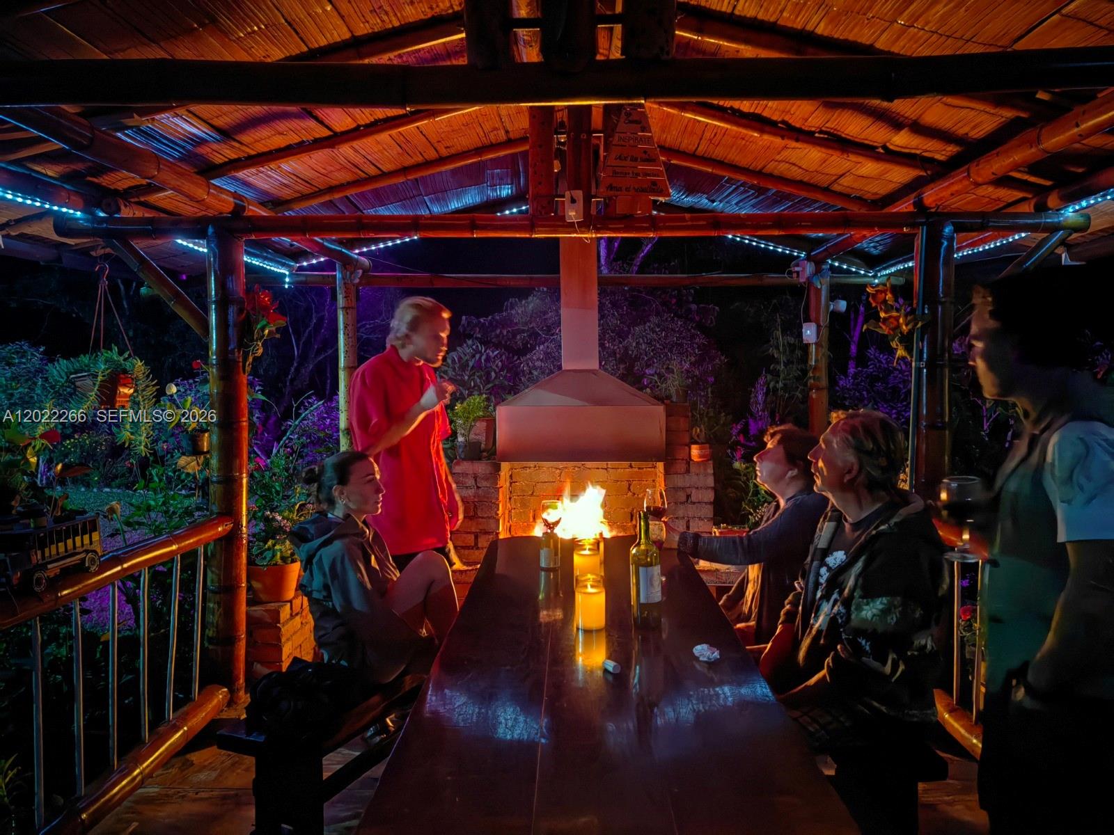 A group of people sits at a long wooden table under a bamboo-roofed outdoor pavilion — X Carretera, 00000, FL
