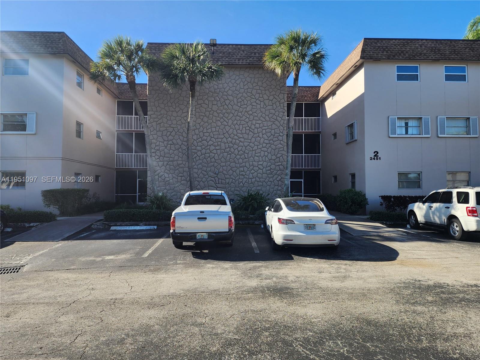 A three-story apartment building exterior features a stone facade, palm trees, and a parking lot — 2451 SW 82nd Ave # 309, Davie FL 33324, DAVIE, FL
