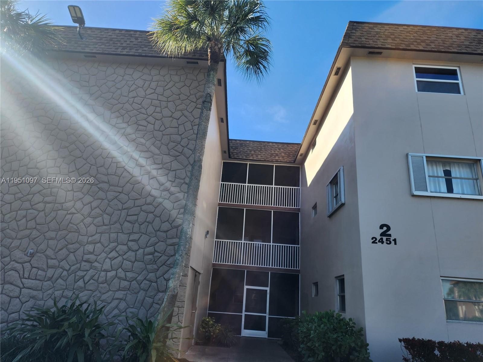 The exterior of a multi-story apartment building features stone veneer, screened balconies, and a palm tree — 2451 SW 82nd Ave # 309, Davie FL 33324, DAVIE, FL