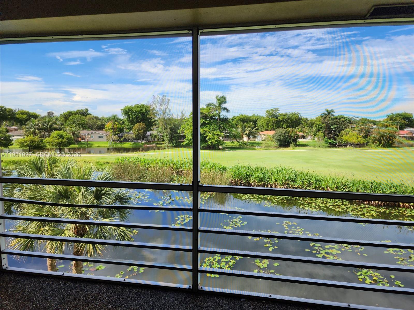 A screened-in balcony overlooks a pond, lush vegetation, and a golf course under a blue sky — 2451 SW 82nd Ave # 309, Davie FL 33324, DAVIE, FL