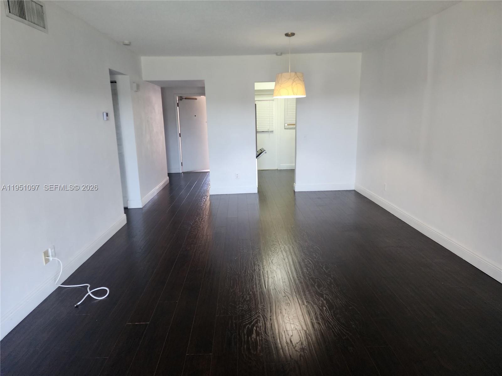 An empty room features dark hardwood floors, white walls, and a single hanging pendant light — 2451 SW 82nd Ave # 309, Davie FL 33324, DAVIE, FL
