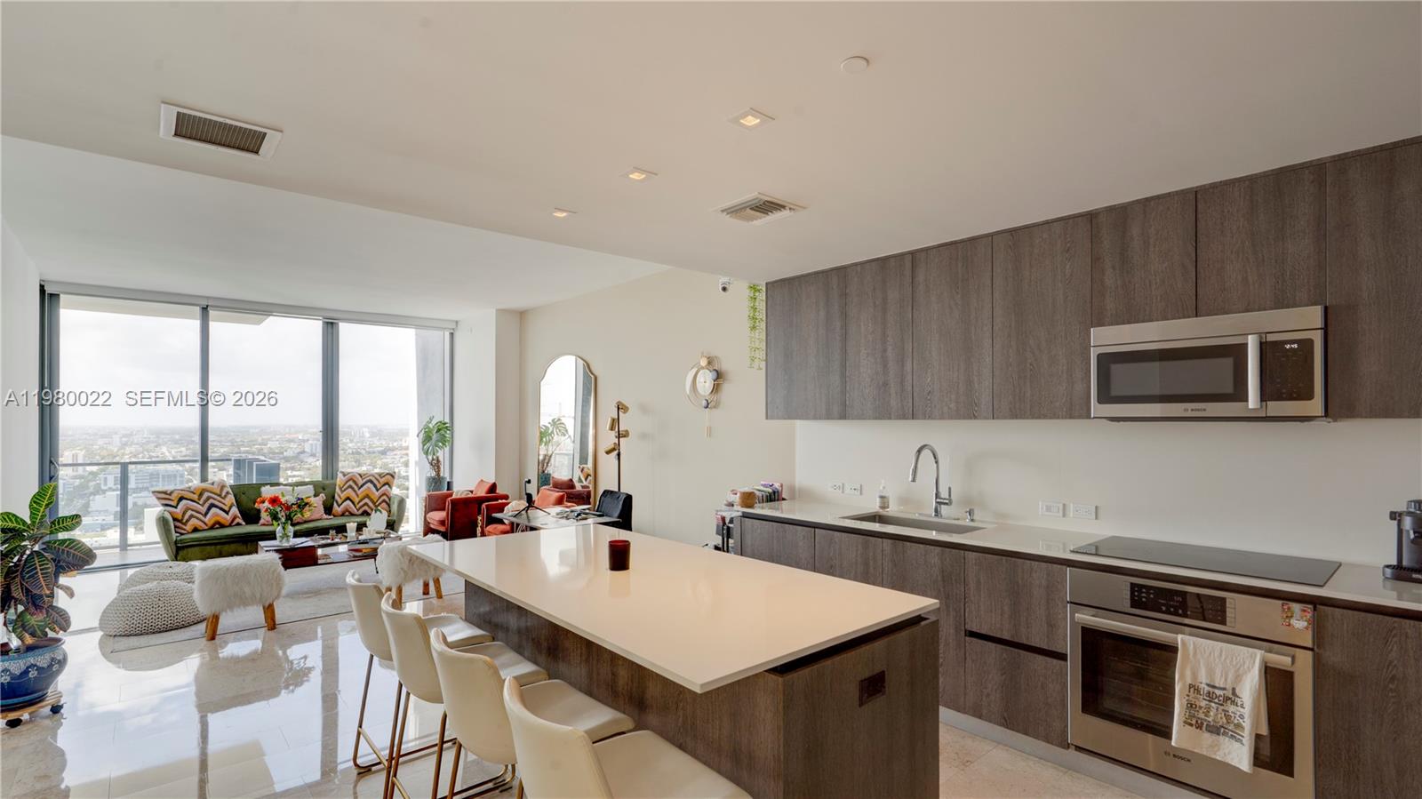 A modern open-concept kitchen and living area features dark wood cabinetry, a white island, and floor-to-ceiling windows — 88 SW 7th St # 2706, Miami FL 33130, MIAMI, FL