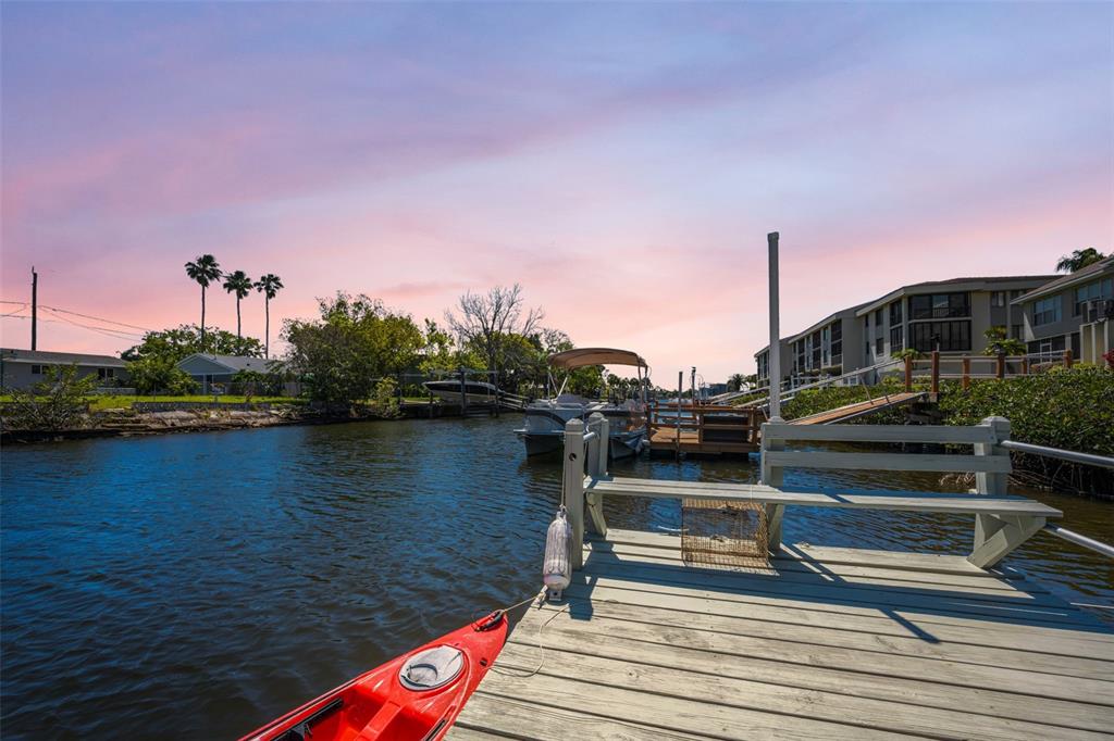 A red kayak is docked at a wooden pier overlooking a canal with boats — 8238 AQUILA STREET, PORT RICHEY, FL