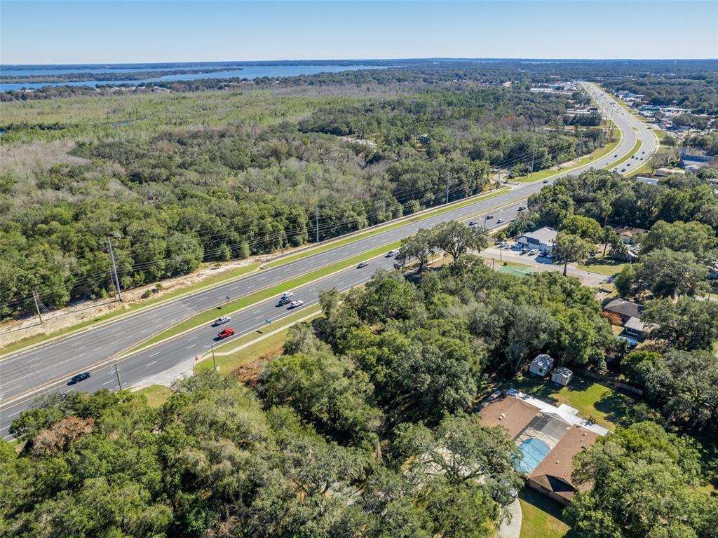 An aerial view shows a house with a pool surrounded by trees near a highway — 0000 US HWY 27/441, FRUITLAND PARK, FL