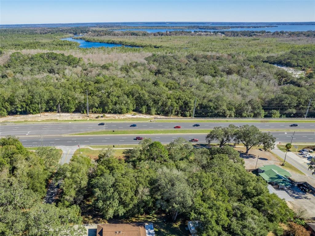 An aerial view shows a multi-lane highway running through a wooded area near a lake — 0000 US HWY 27/441, FRUITLAND PARK, FL