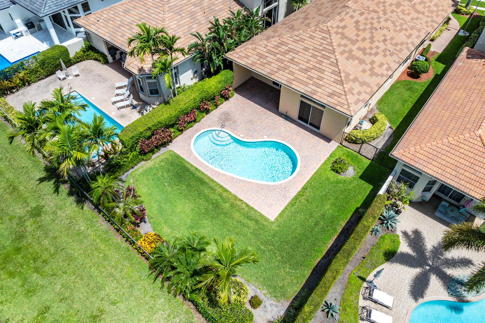 An aerial view shows a backyard with a kidney-shaped pool, patio, and landscaped lawn — 8102 Valhalla Drive, Delray Beach FL 33446, DELRAY BEACH, FL