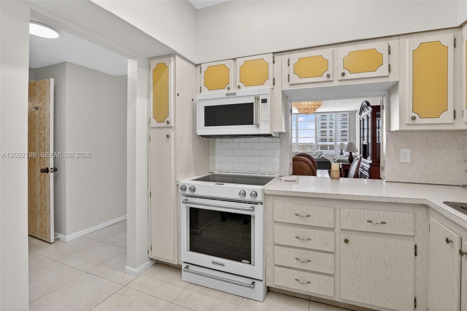 A kitchen features white cabinets with yellow accents, a white stove, and a pass-through window — 1817 S Ocean Dr # 19, Hallandale Beach FL 33009, HALLANDALE BEACH, FL